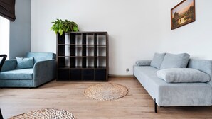 Ein modernes Wohnzimmer mit einem blauen Sofa, einem grauen Sofa, Holzboden, einem gewebten Teppich und einer Pflanze auf einer Regaleinrichtung.