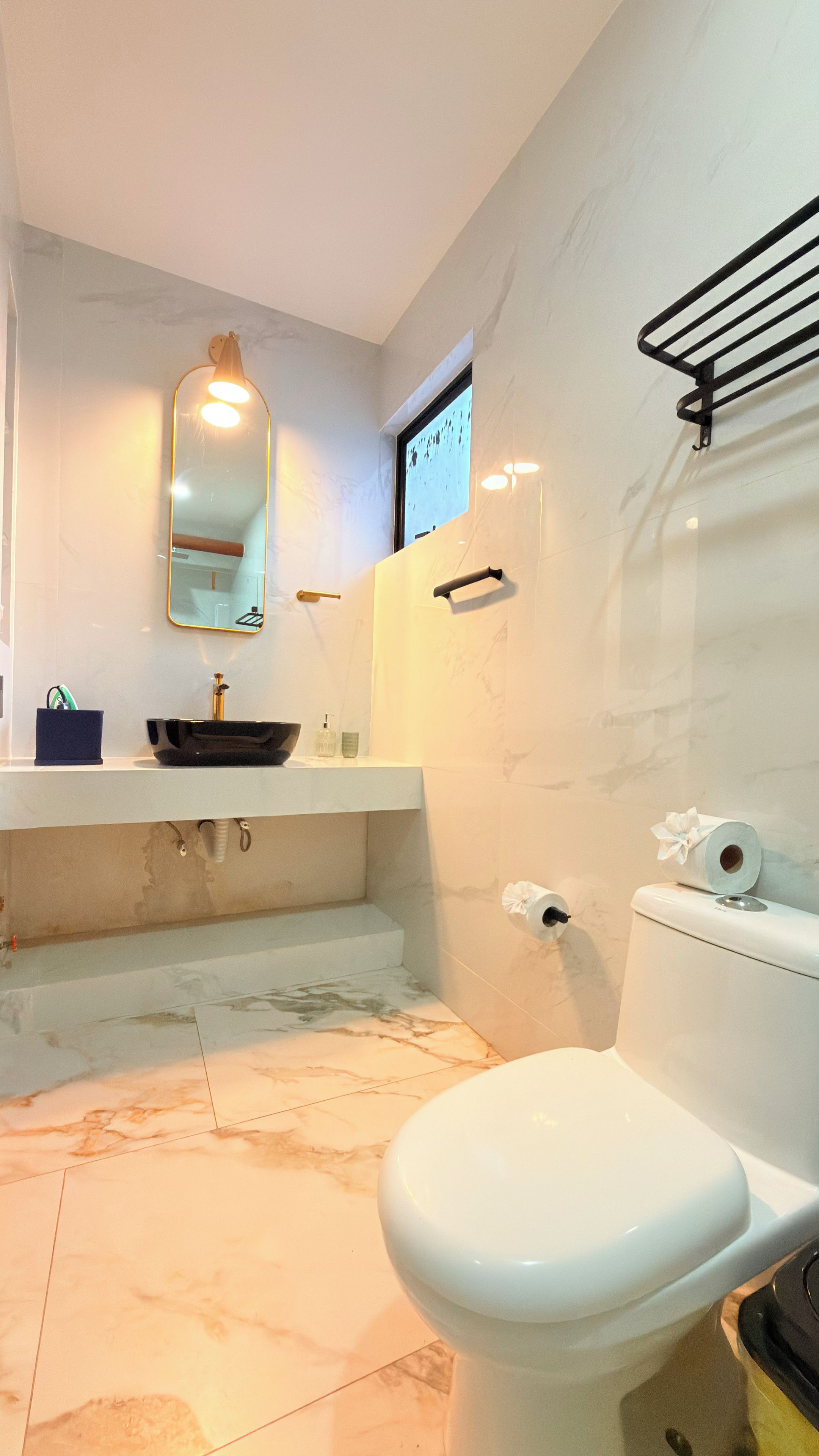 Un baño con inodoro blanco, lavabo con recipiente, espejo y una pequeña ventana.