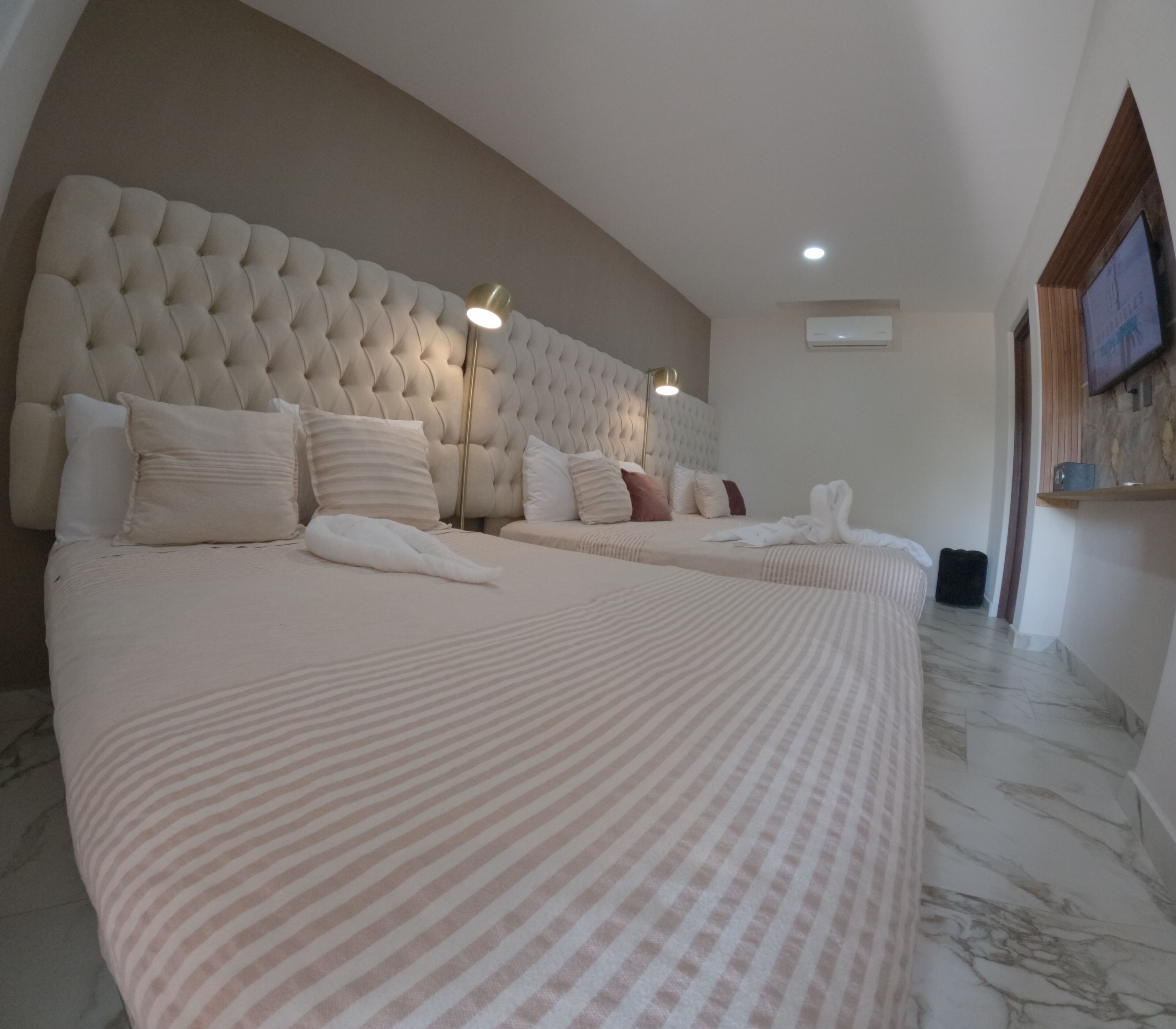 Un dormitorio amplio y moderno con cabecera capitonada, varias camas y suelo de mármol.