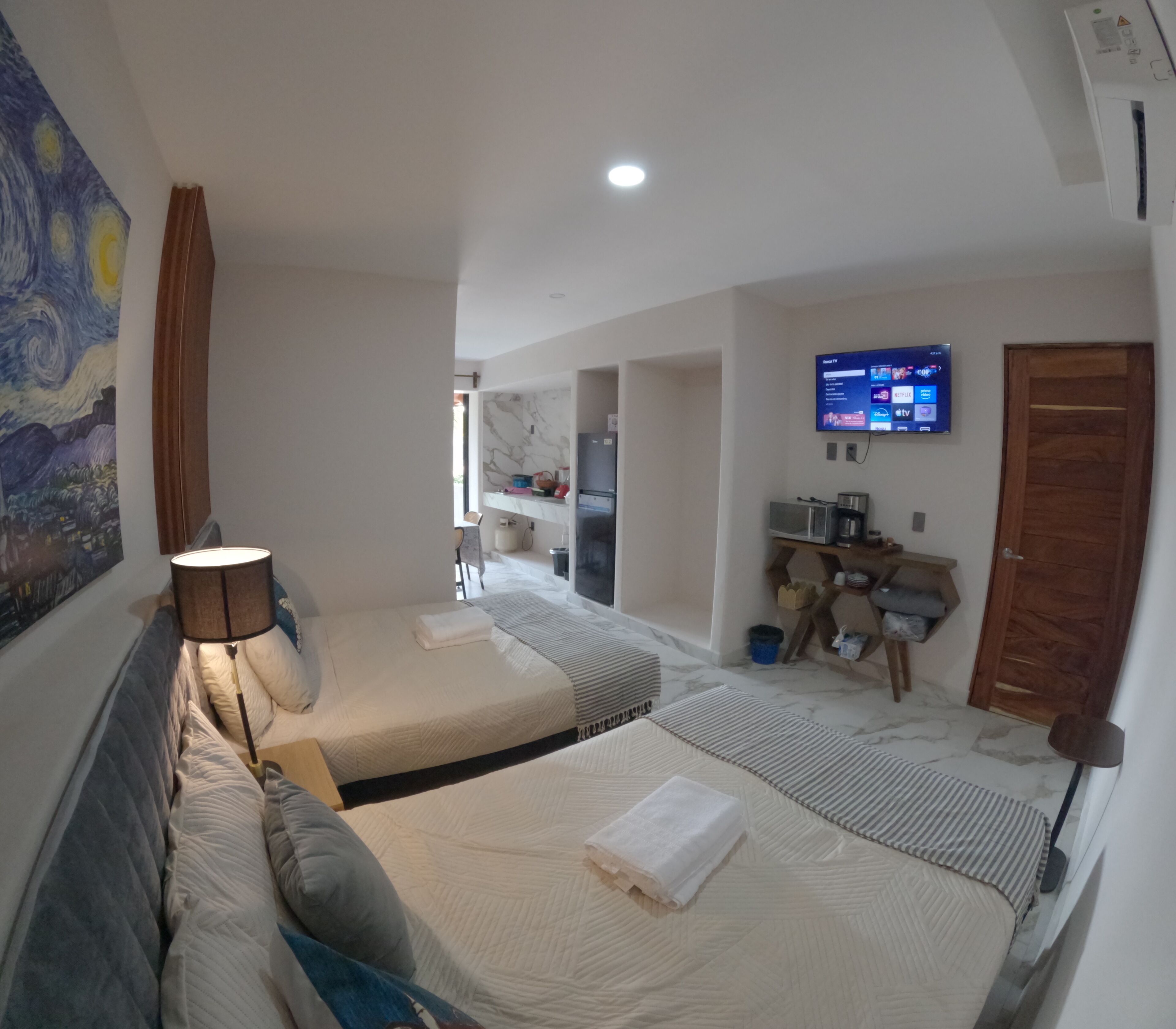 A hotel room with two beds, a TV, a painting, and a kitchenette.