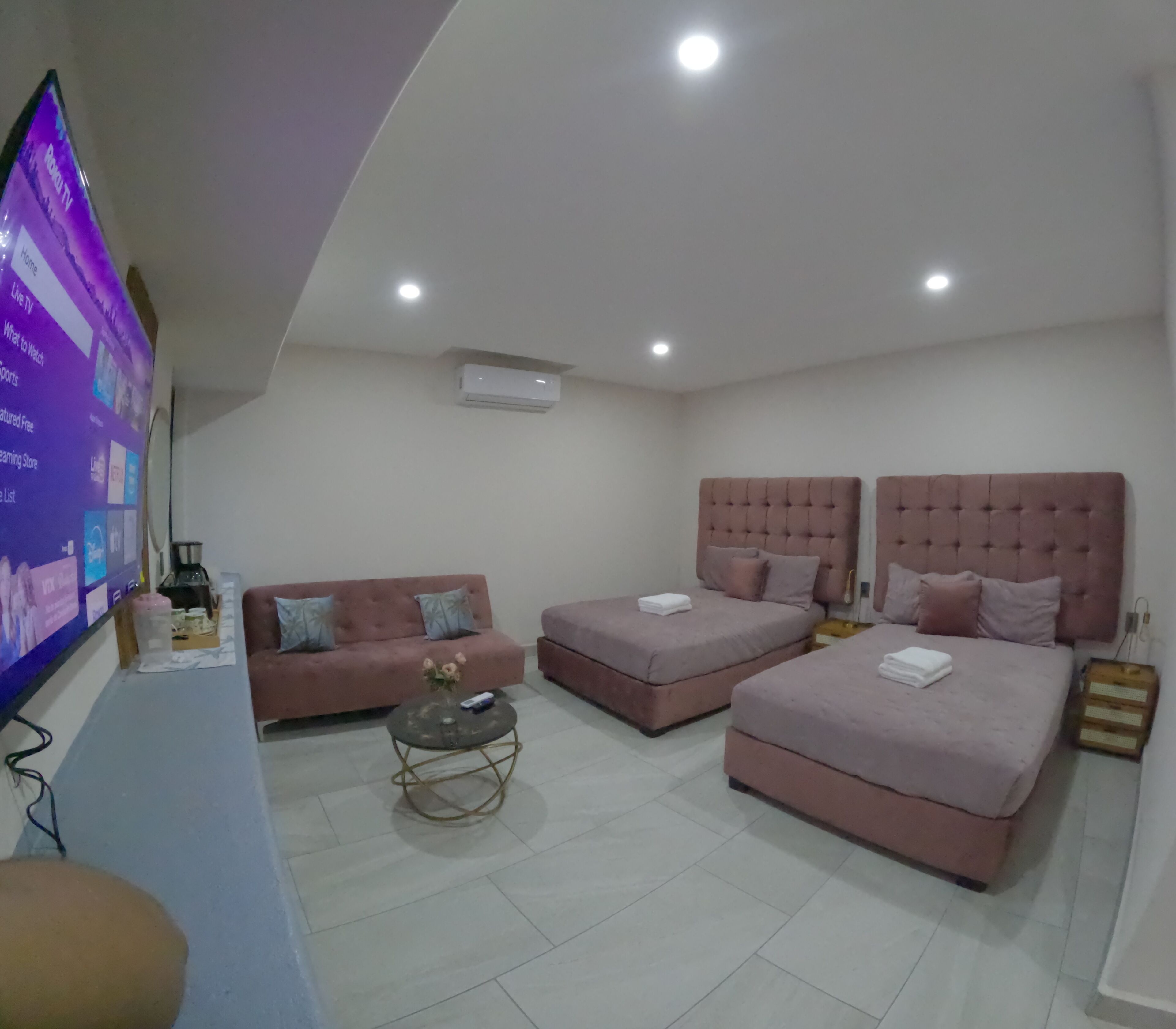 Ein modernes Hotelzimmer mit zwei Betten, einem Sofa, einem Couchtisch und einem an der Wand befestigten Fernseher.