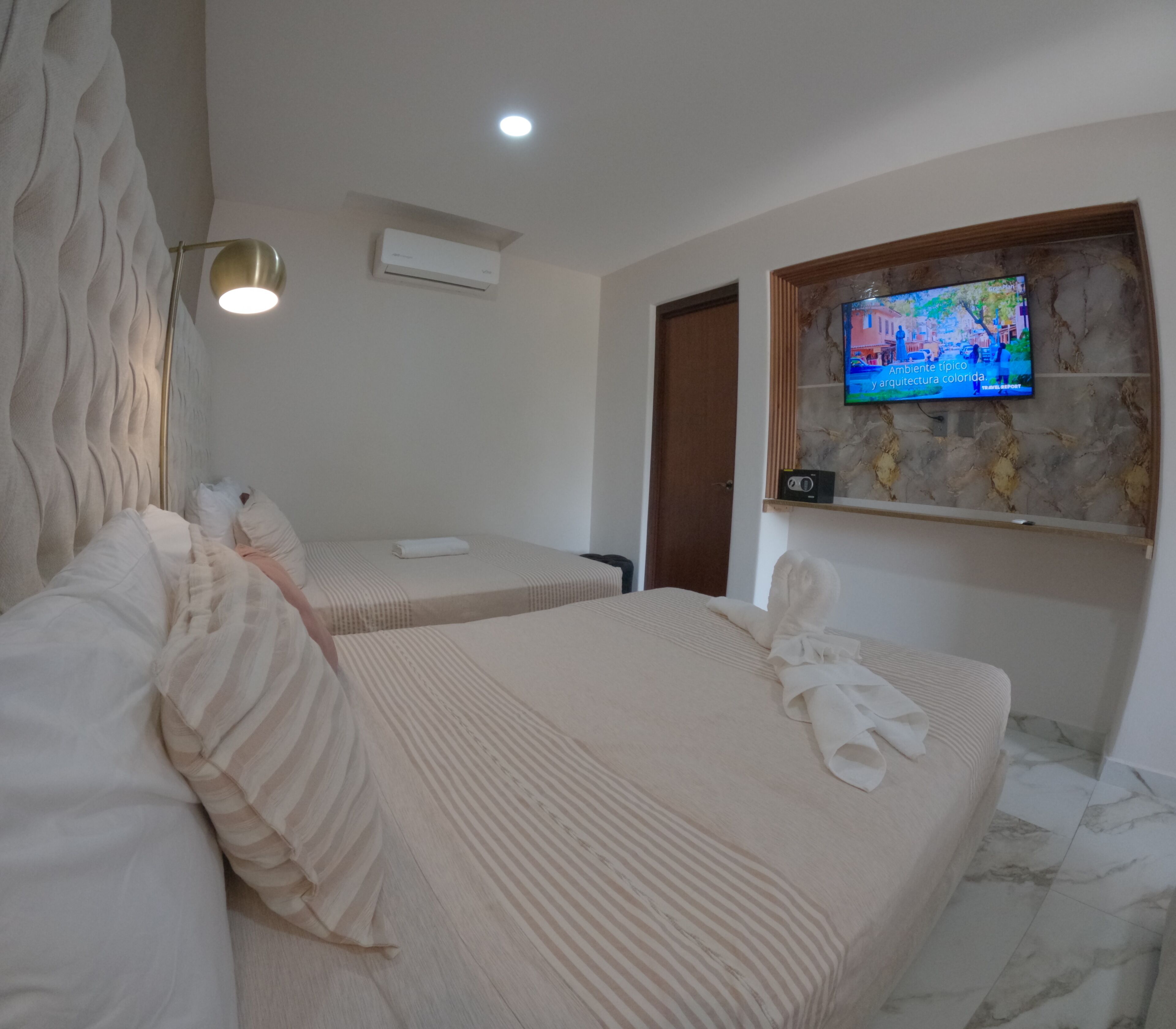 Ein Hotelzimmer mit zwei Betten, einem an einer Marmorwand befestigten Fernseher und einer Klimaanlage unter der Decke.