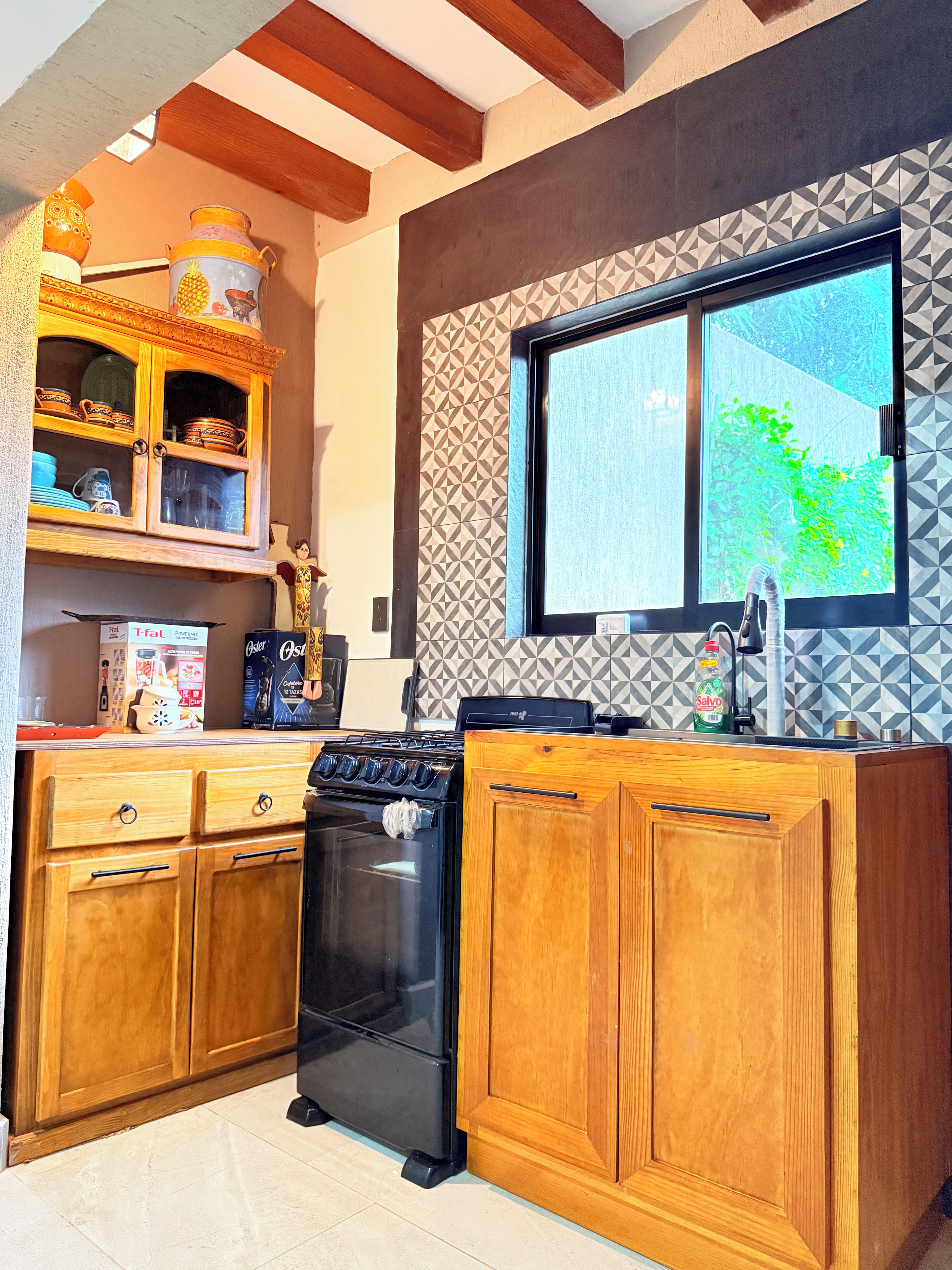 A kitchen with wooden cabinets, a black stove, and a window with a geometric backsplash.
