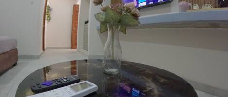 A living room with a round glass coffee table, a remote control, and a vase with flowers.