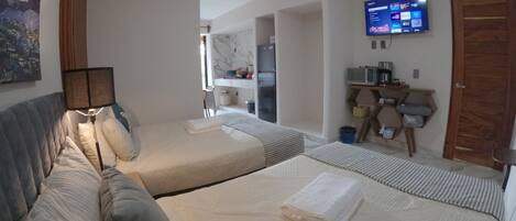 Habitación de hotel con dos camas, televisión, kitchenette y baño.