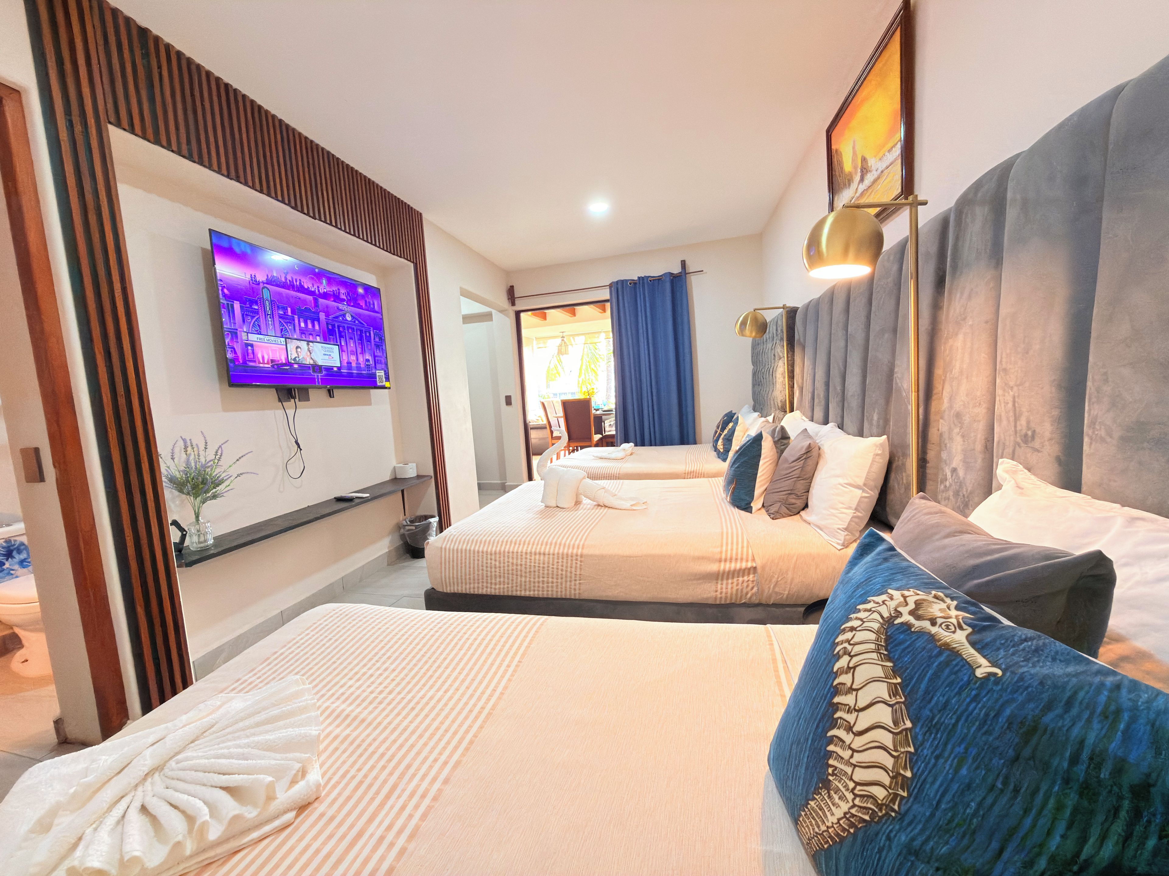 Habitación de hotel con dos camas, un televisor en la pared, una mesita de noche y un ventanal con cortinas.