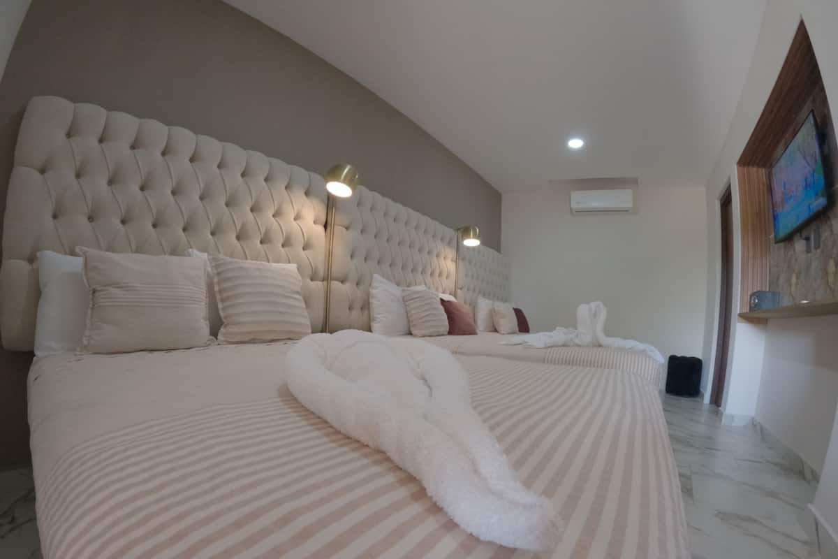 A spacious bedroom with a large bed, a tufted headboard, and a flat-screen TV mounted on the wall.