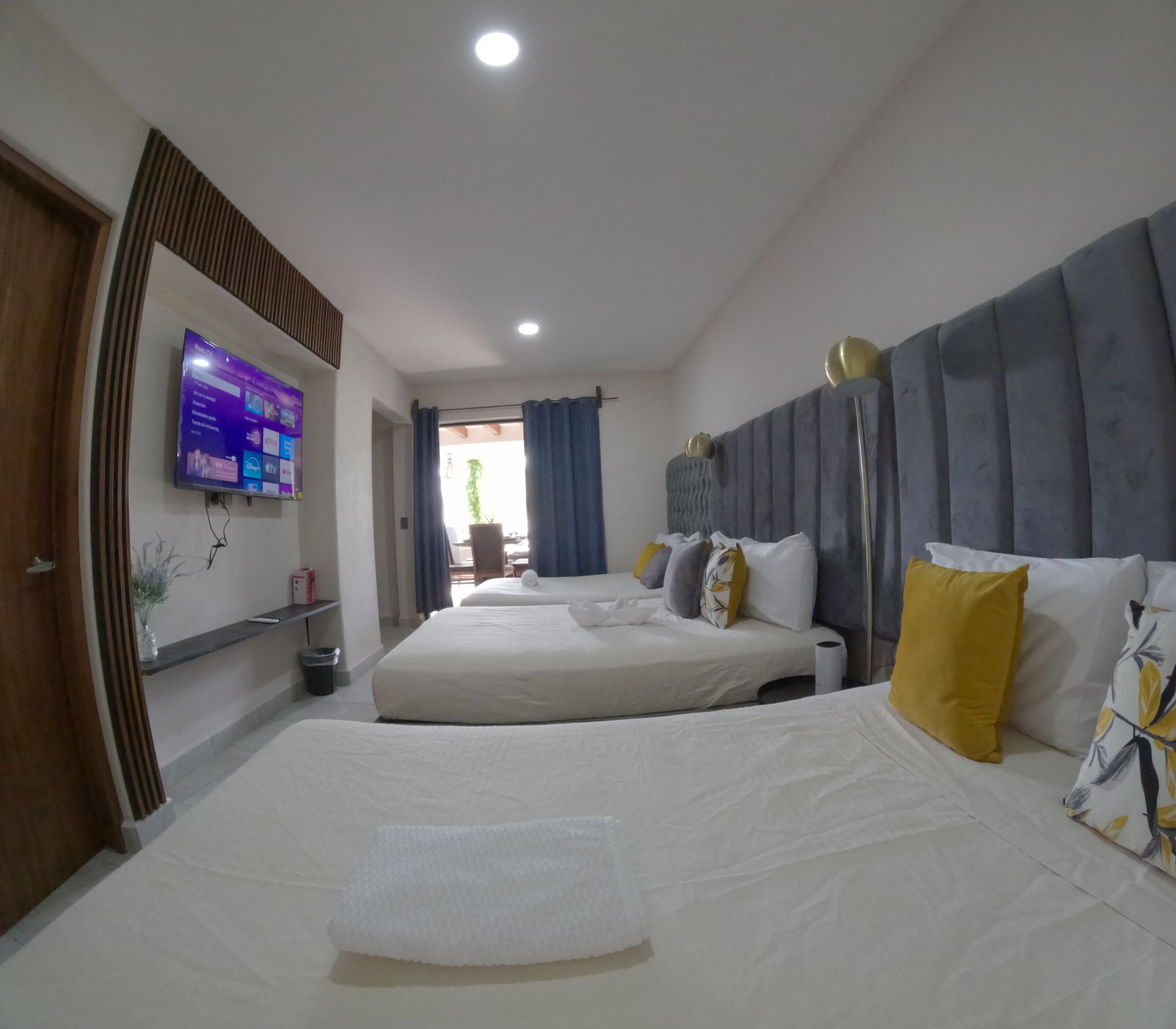 A hotel room with two beds, a flat-screen TV mounted on the wall, and a large window with curtains.