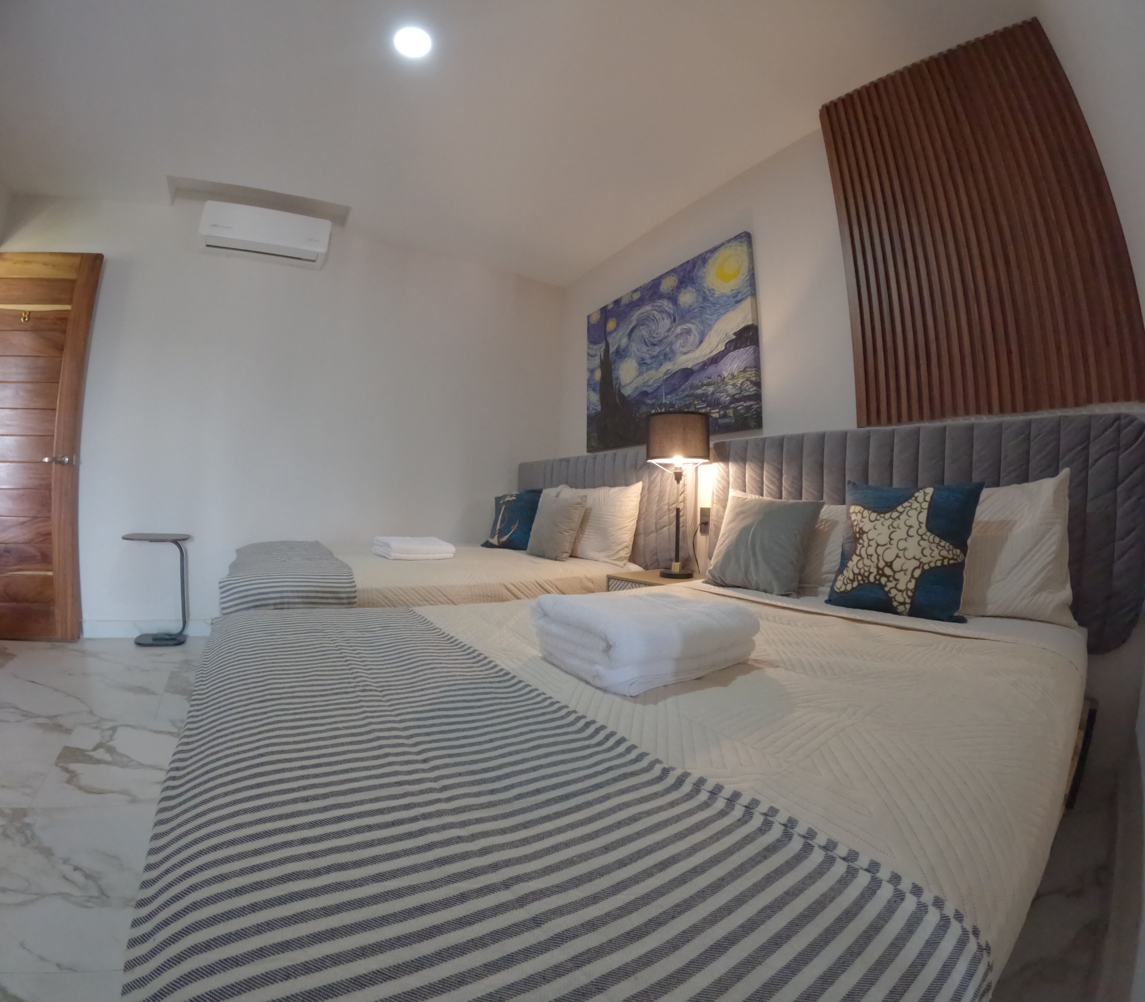 A hotel room with two beds, a painting on the wall, a lamp, and a wooden door.