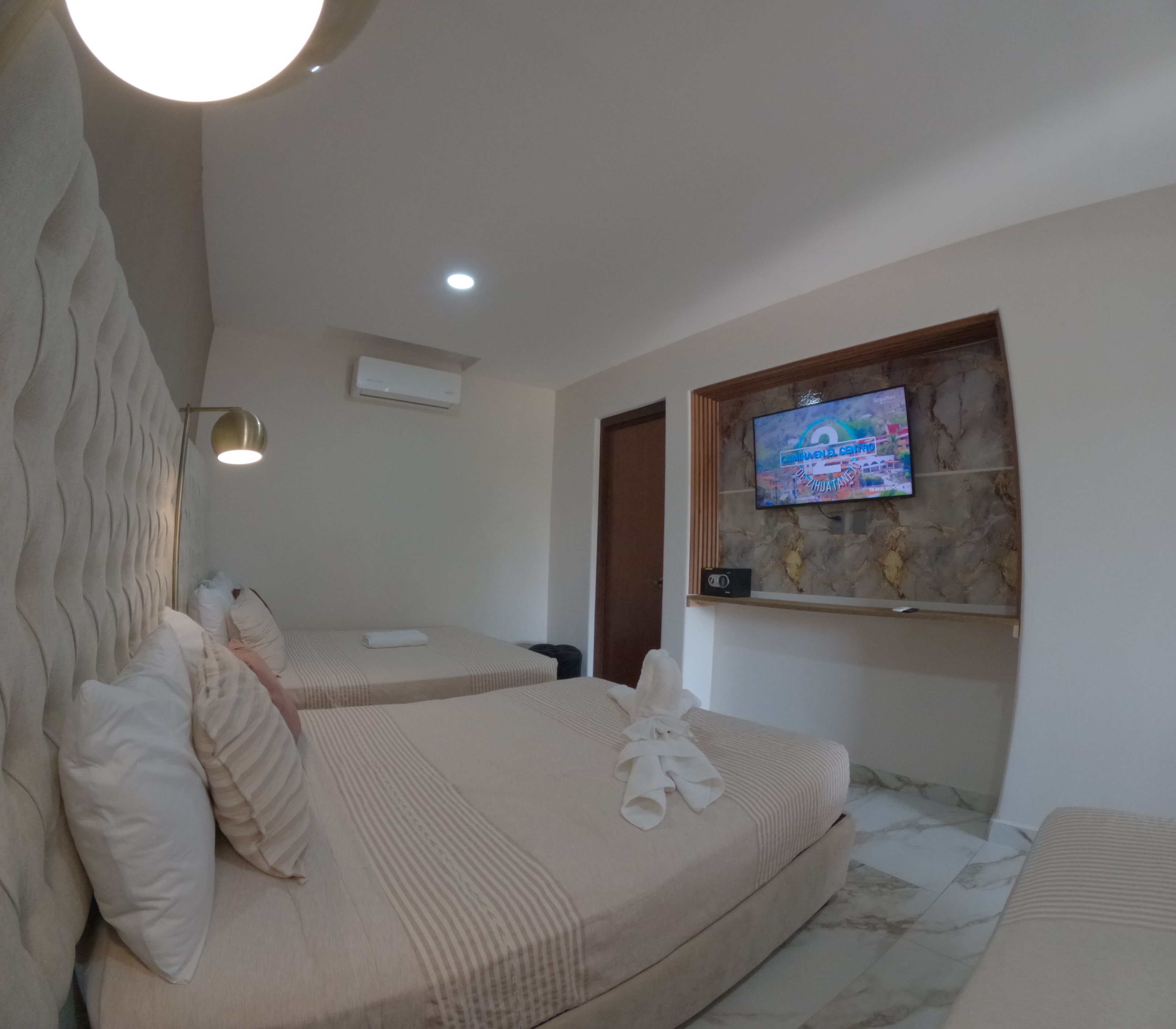 A bedroom with two beds, a TV mounted on a stone wall, an air conditioning unit, and a lamp.