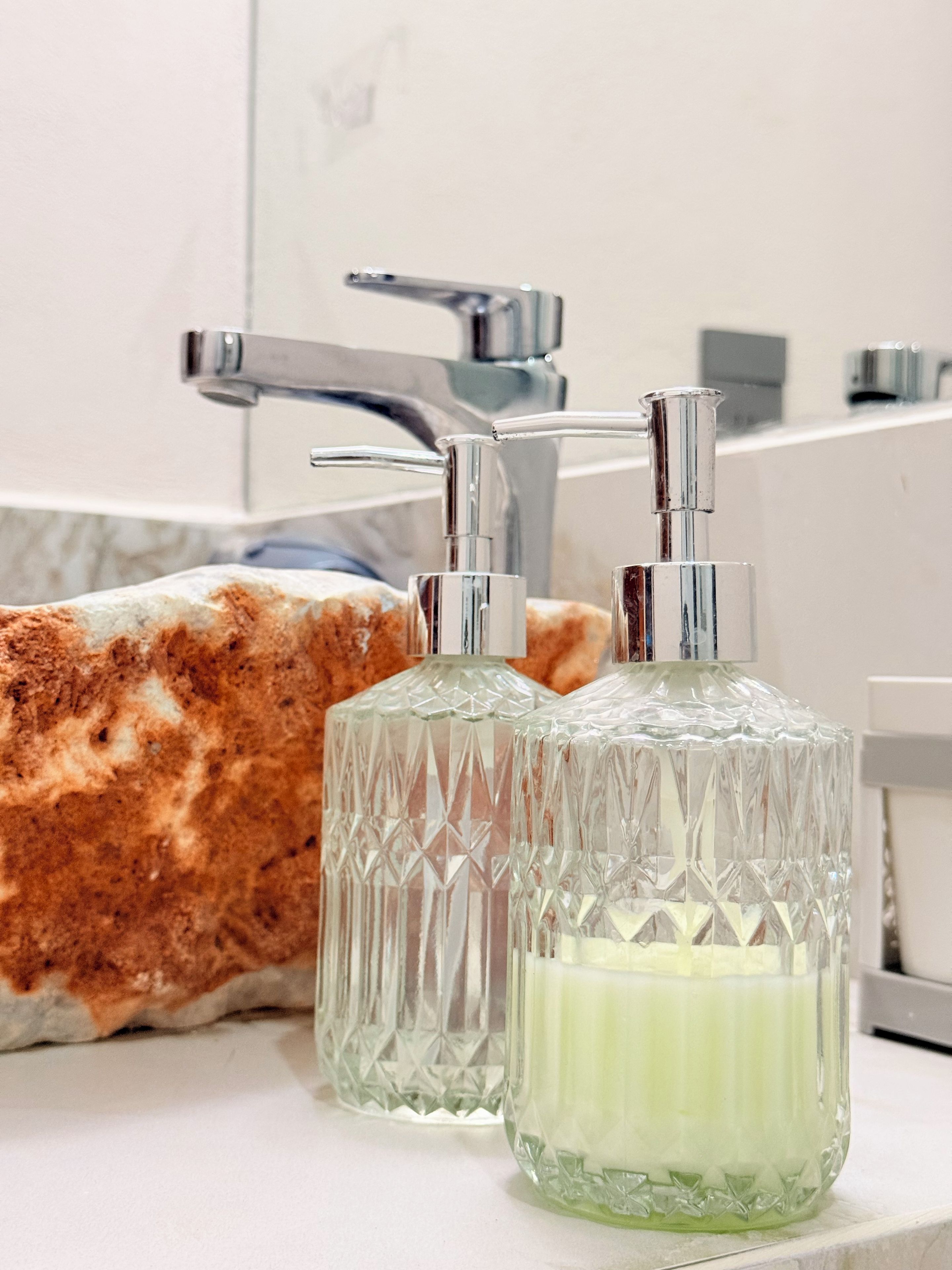 Un baño con un grifo moderno y dos dispensadores de jabón de vidrio sobre una encimera de mármol.