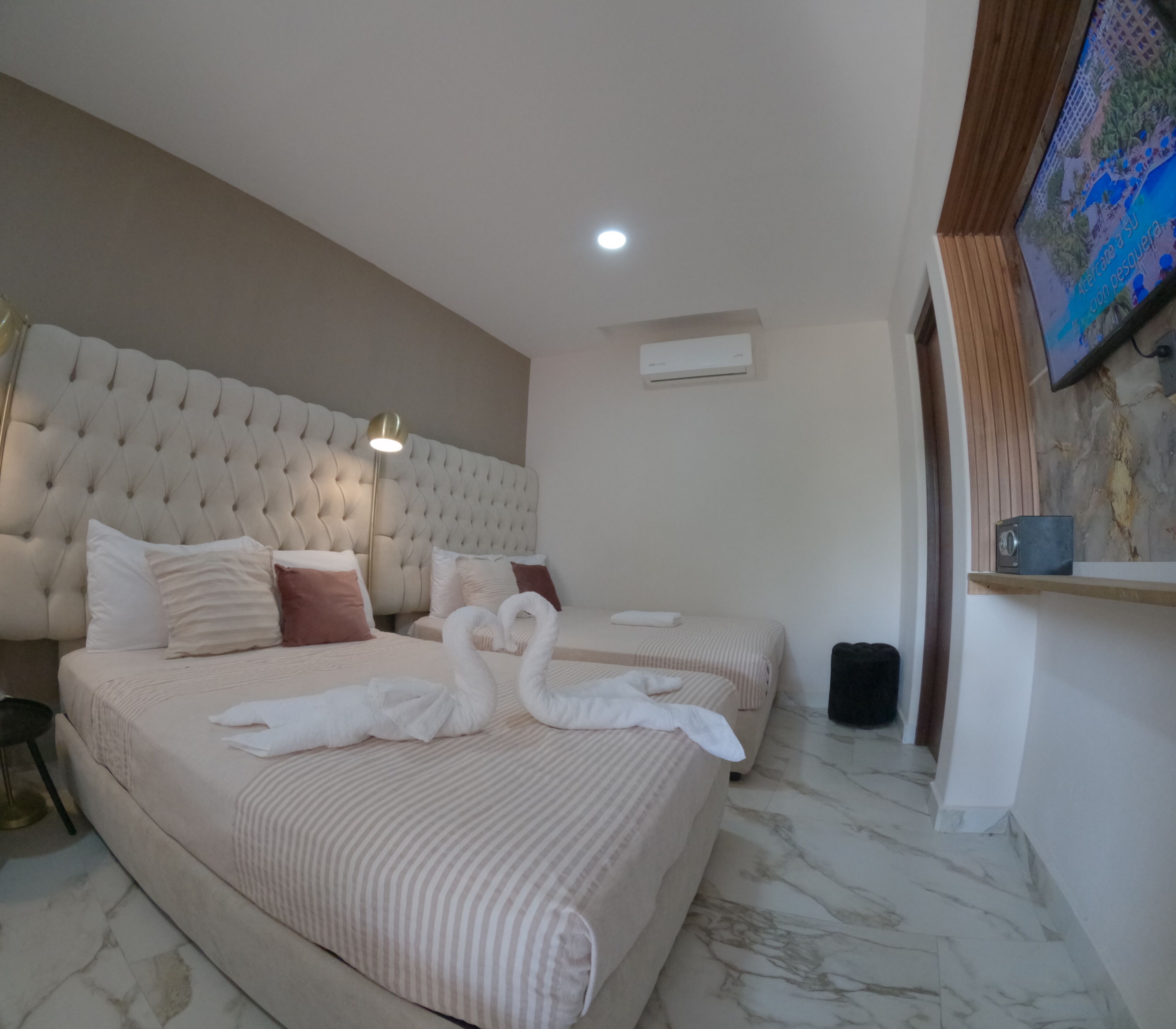 Habitación de hotel con dos camas, un cabecero grande tapizado, un televisor de pantalla plana y suelo de mármol.