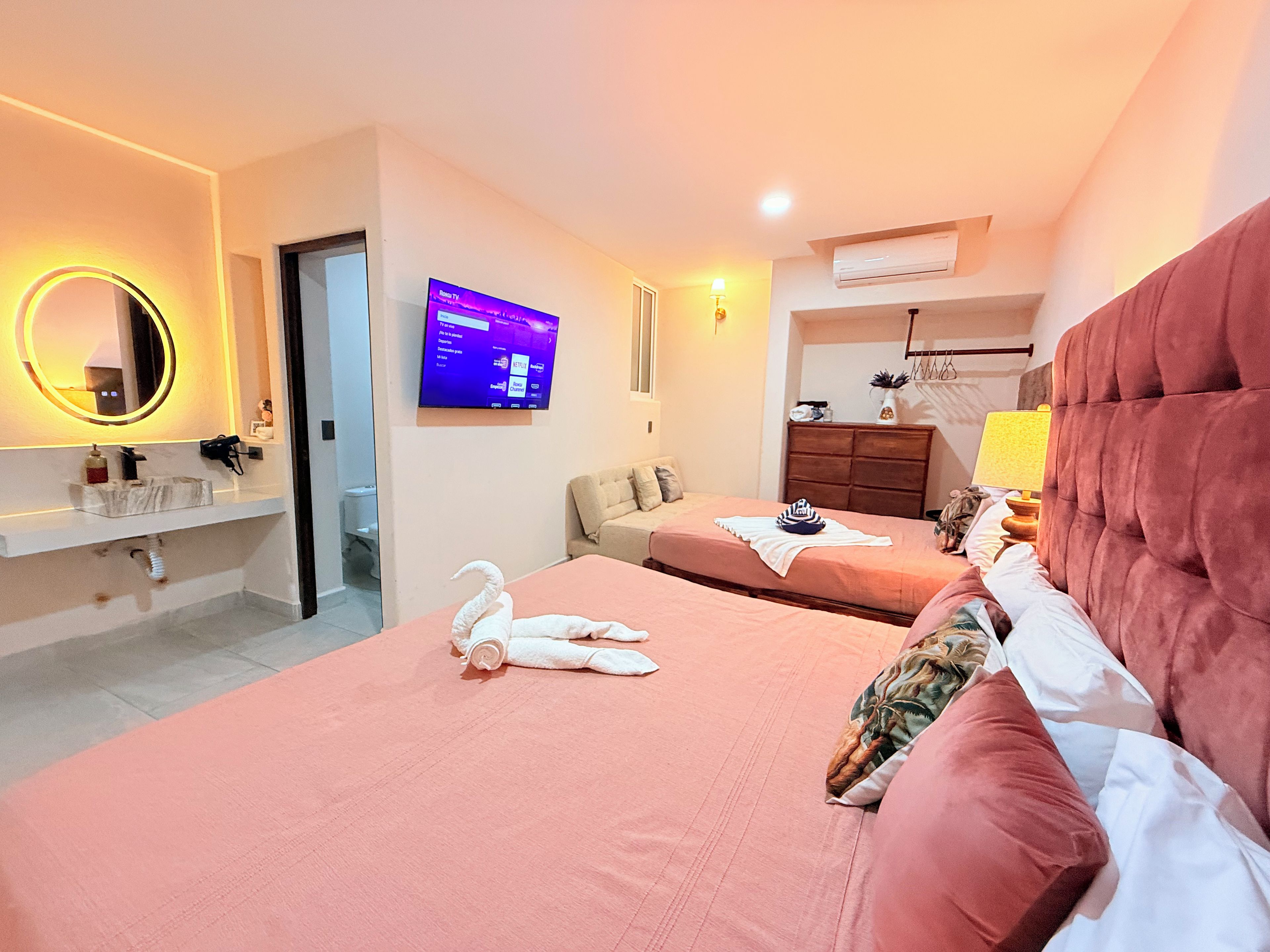 Habitació d'hotel amb dos llits, un televisor, un mirall, una tocador i un bany.