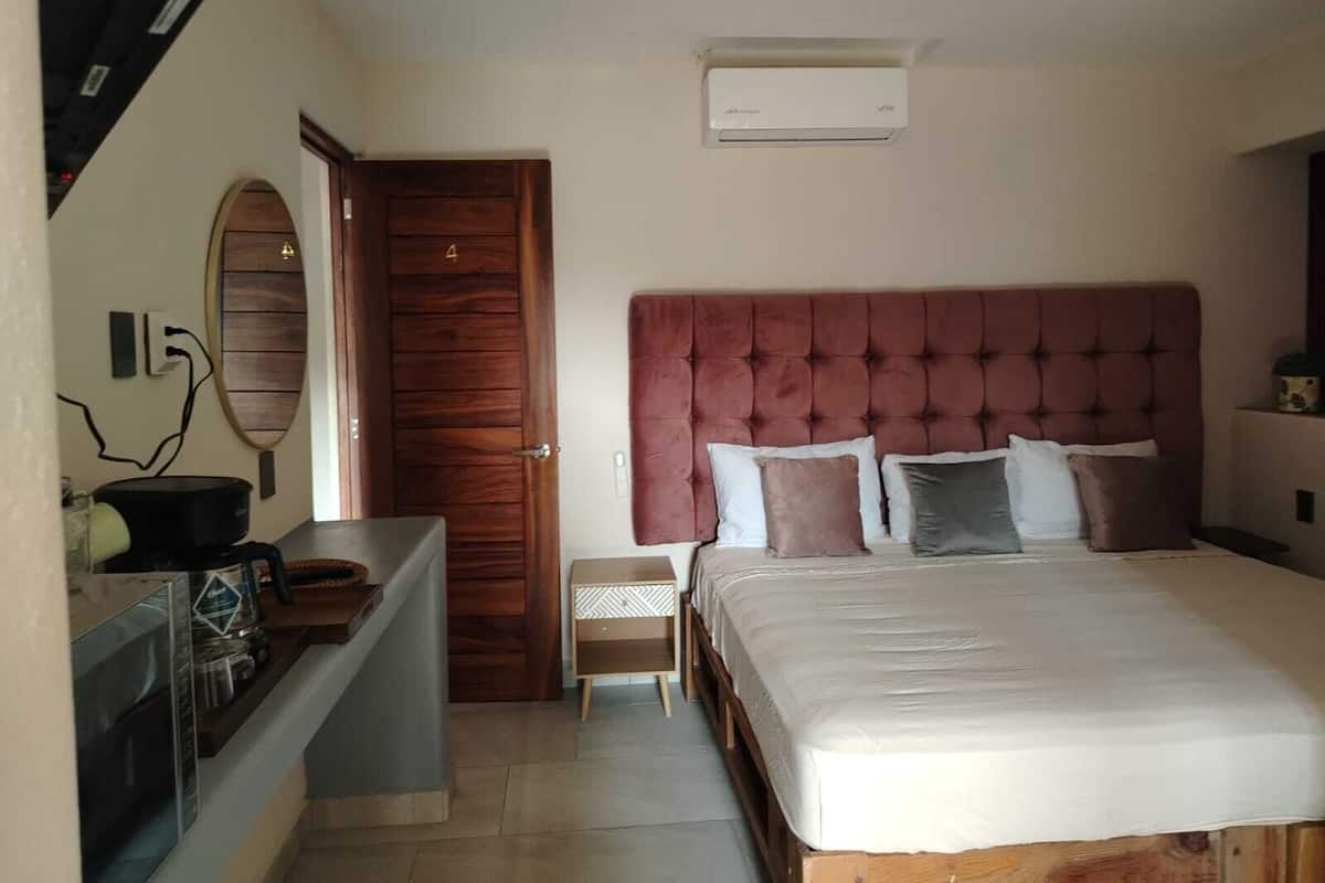 A bedroom with a large bed, a wooden door, a small bedside table, and a wall-mounted air conditioner.
