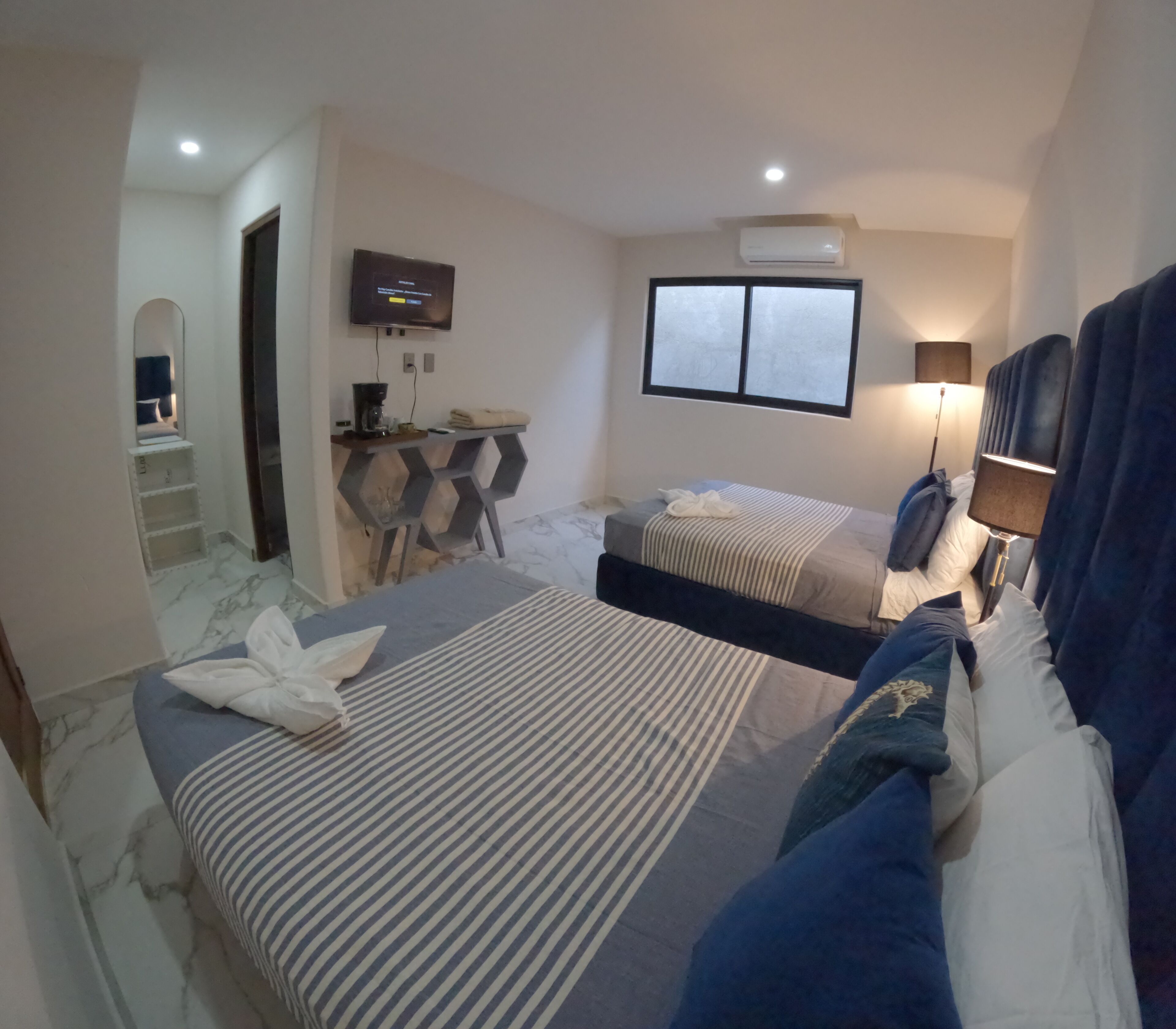 Une chambre d’hôtel avec deux lits, une télévision, une fenêtre et un bureau avec une lampe.
