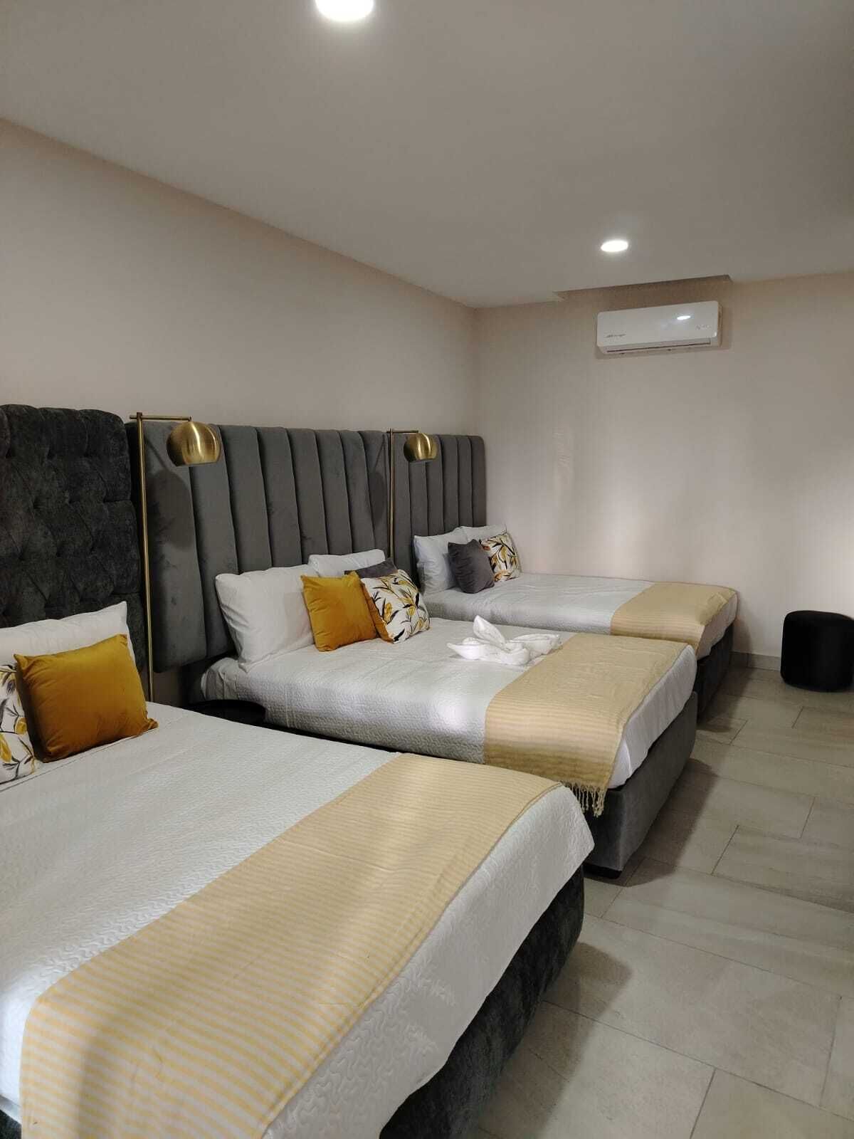 Ein Hotelzimmer mit drei Betten, einem modernen Kopfteil und einer Wand-Klimaanlage.