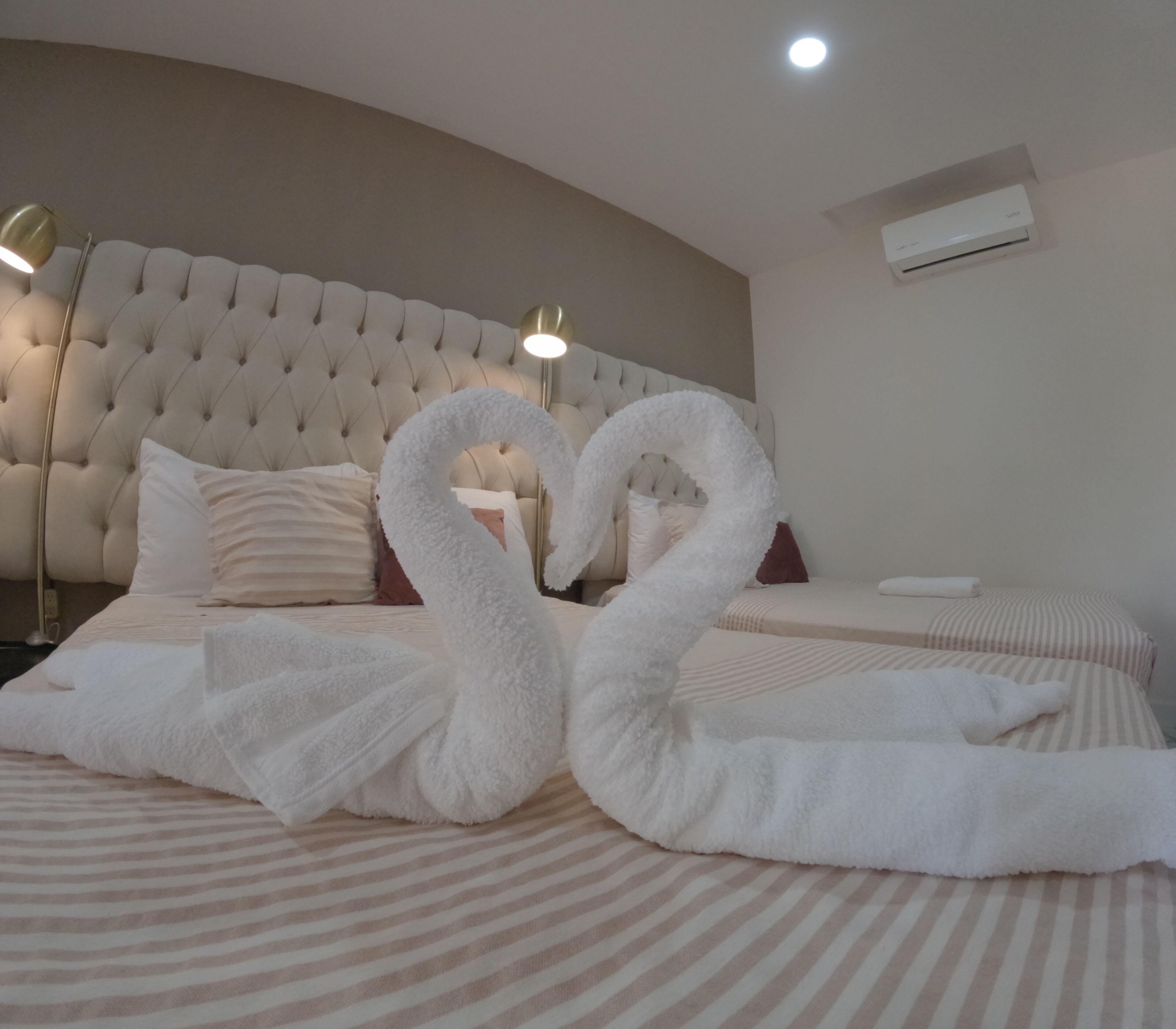 Una habitación de hotel con una cama grande, cabecera capitonada y aire acondicionado instalado en la pared.