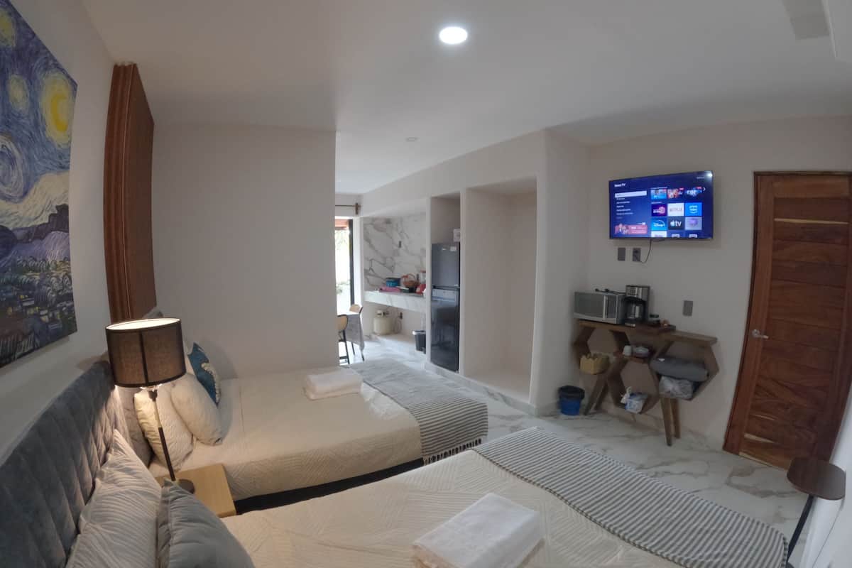 A hotel room with two beds, a TV, a desk, and a bathroom visible in the background.