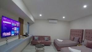A modern hotel room with a flat-screen TV displaying a streaming service interface, a sofa, two beds, a small round table, and a ceiling-mounted air conditioner. - Espacio Diez Hotel Boutique (Zihuatanejo)