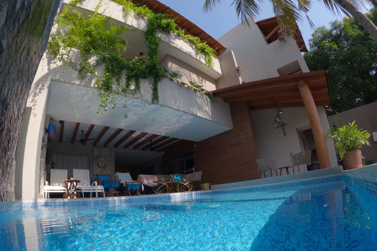 A swimming pool with a tiled edge, surrounded by lounge chairs and a covered patio area.