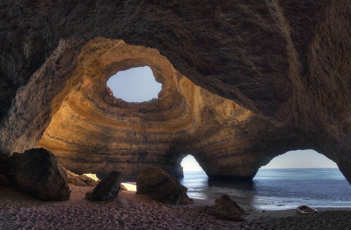 A natural rock formation with a circular opening, a sandy beach, and the ocean in the background.