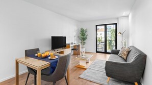 Una sala de estar moderna con comedor, un televisor de pantalla plana, una planta en maceta y un sofá con cojín estampado.