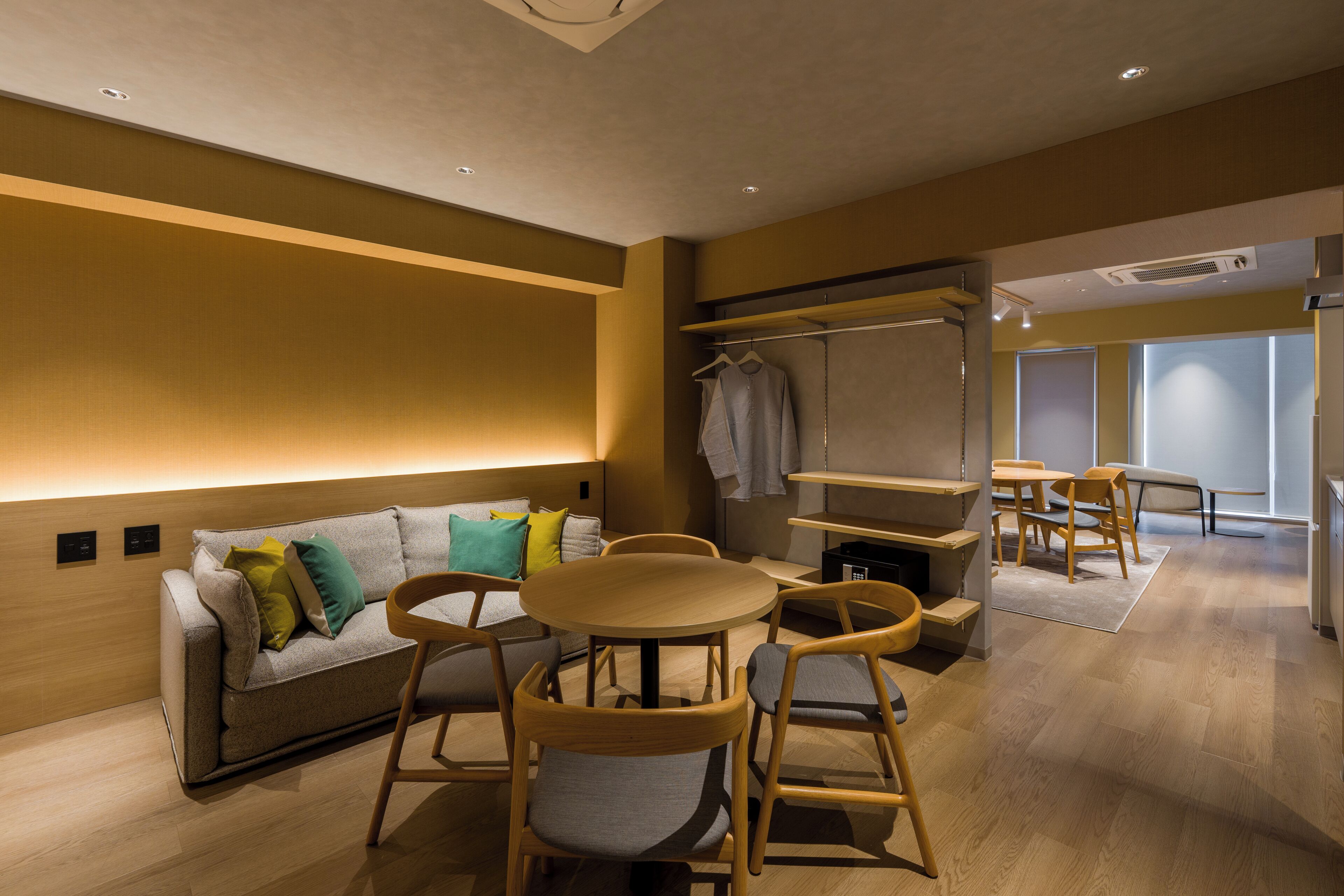 A modern hotel room with a sofa, chairs, a small table, and a wardrobe.