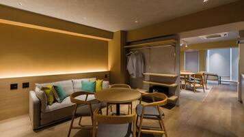 A modern hotel room with a sofa, chairs, a small table, and a wardrobe.