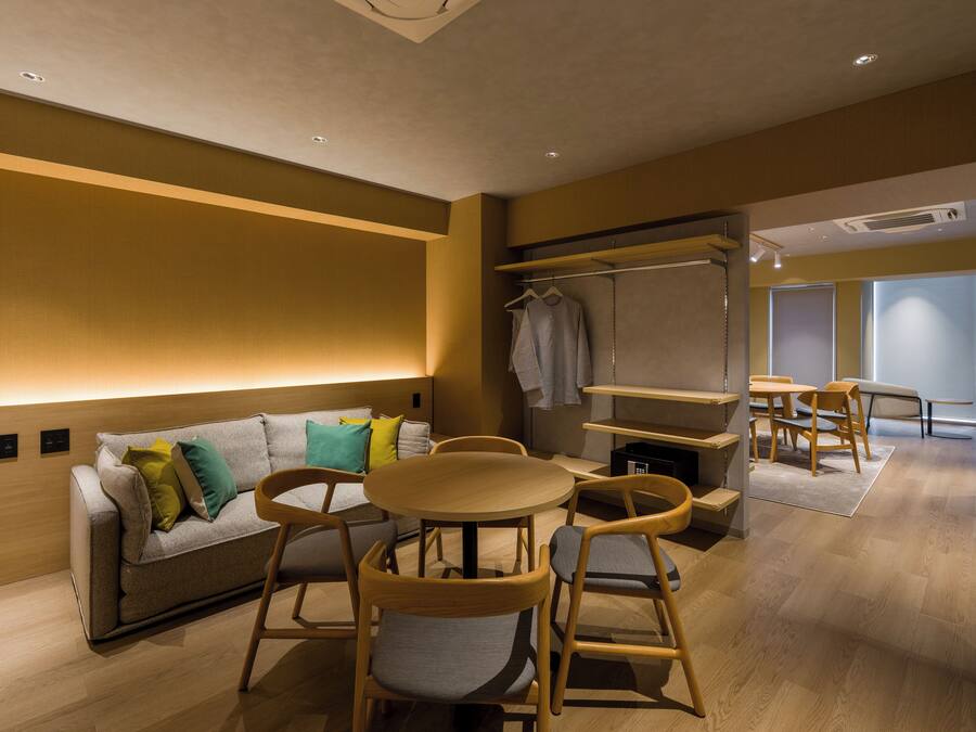 A modern hotel room with a sofa, chairs, a small table, and a wardrobe.