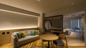 A modern living room with a sofa, a round table, and chairs. There is a coat rack with hanging clothes. - Sumu Ueno East (Tokyo)