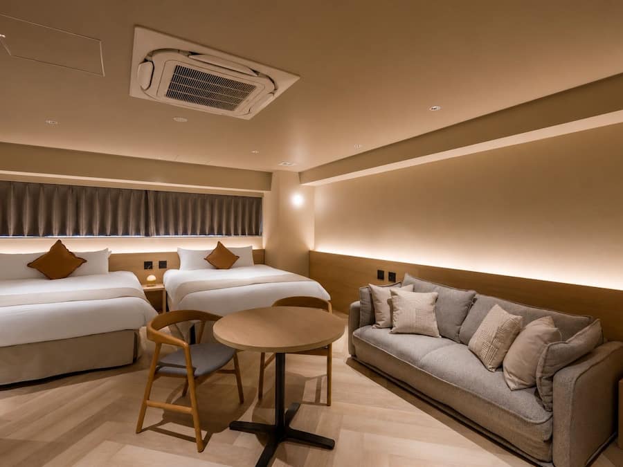 A hotel room with a bed, two bedside tables, a sofa, a round table, and a chair.