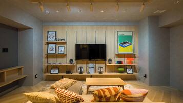 A modern living room with a large flat-screen TV, wooden shelves with framed pictures, and a comfortable seating area with cushions.