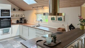 A modern kitchen with white cabinets, a built-in oven, a coffee maker, and a window overlooking greenery. - Beautiful home in Idestrup with sauna (Idestrup)