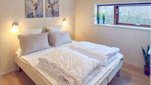 A neatly made bed with white bedding and pillows, a window with plants, and two wall-mounted paintings of deer. - Awesome apartment in Væggerløse with WiFi (Væggerløse)