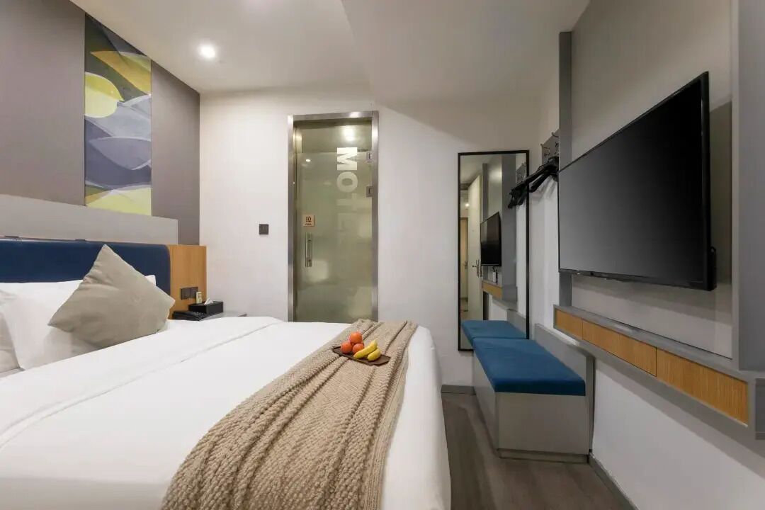 Una habitación de hotel moderna con una cama, una mesita de noche, un televisor y un espejo.