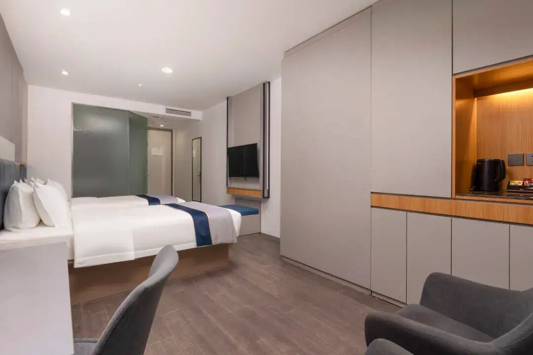 A modern hotel room with a bed, a desk, a chair, a TV, and a coffee machine.