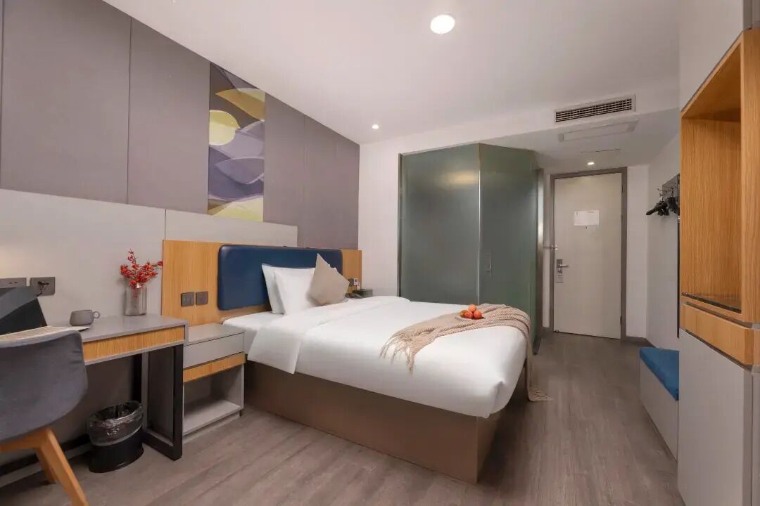 A modern hotel room with a bed, desk, and wardrobe.