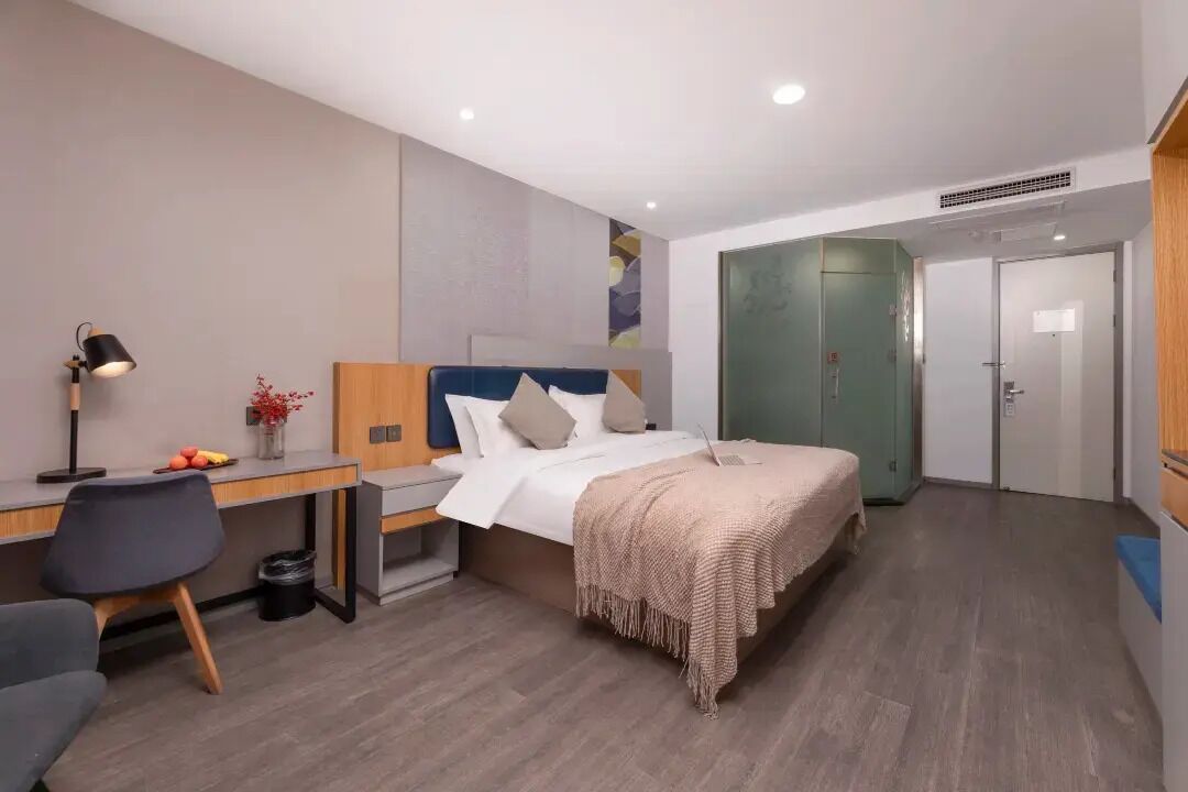 A modern hotel room with a bed, desk, chair, and a small table with fruit.