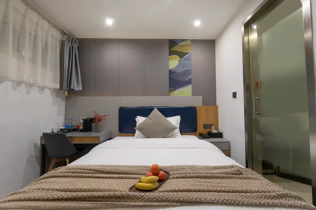 Une chambre d’hôtel avec un lit, un bureau et une chaise. On trouve un panier de fruits sur le lit.