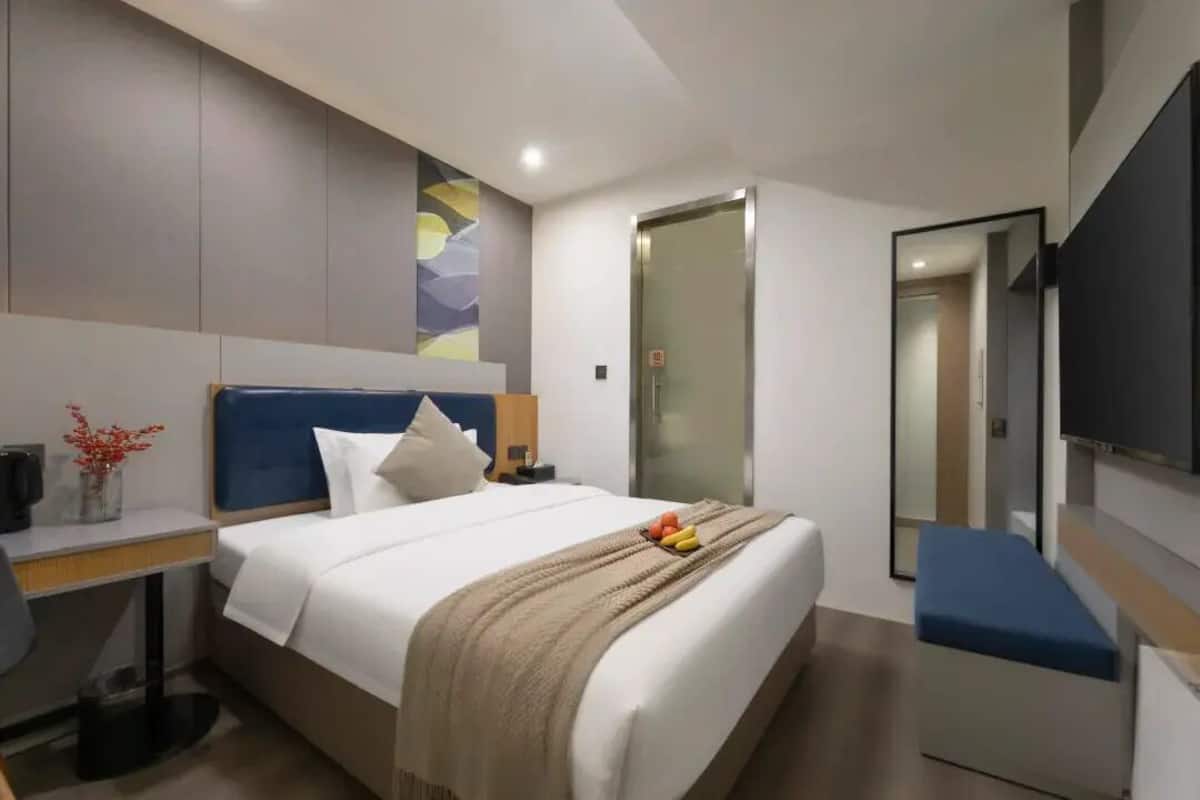 Una camera d'albergo moderna con un letto, un comodino, una TV e uno specchio.