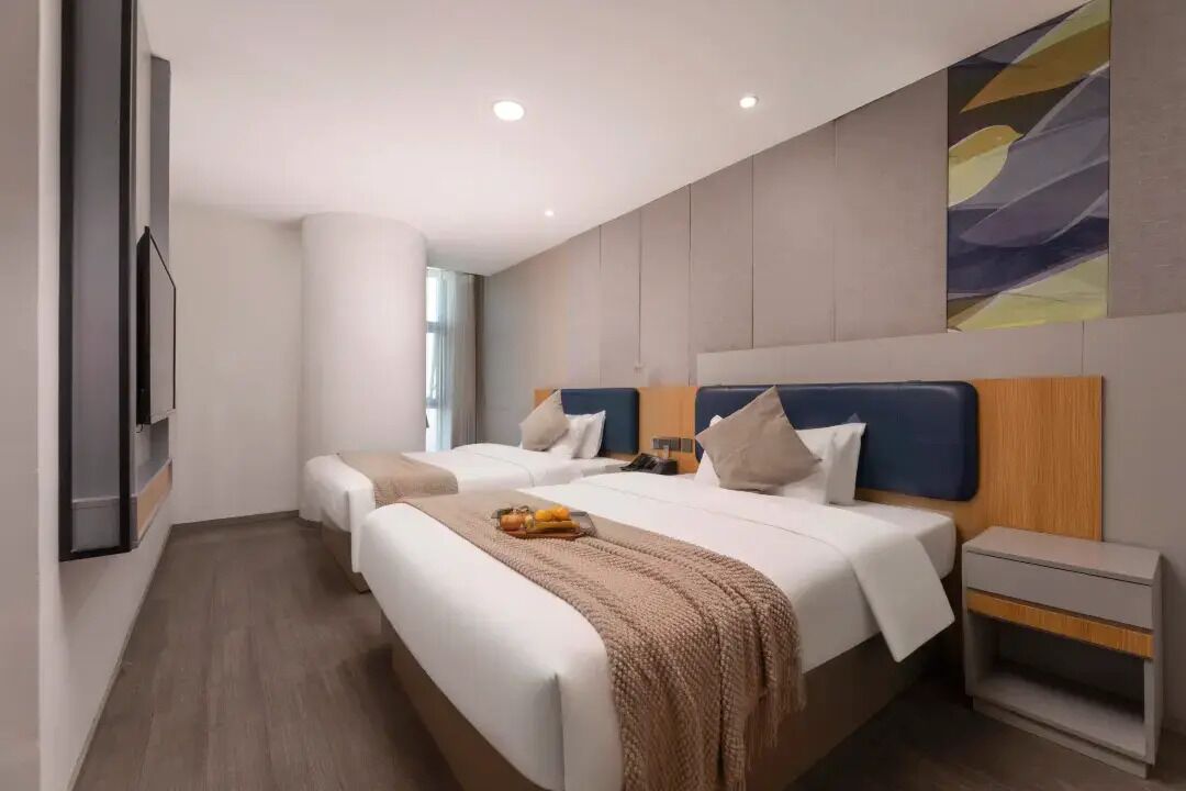 A modern hotel room with two beds, a flat-screen TV, a bedside table, and a large abstract painting on the wall.
