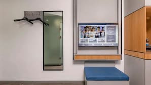 A room with a mounted television displaying a program, a coat rack, and a bench. - suzhouzhexujiajiudian (Suzhou)