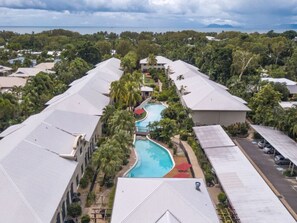 Ein Resort mit einem zentral gelegenen Schwimmbad, umgeben von mehreren Gebäuden mit flachen Dächern, und Blick auf das Meer im Hintergrund.