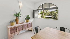 Un comedor con una mesa y sillas de madera, un armario de ladrillo con plantas en macetas y un ventanal de arco que da a un jardín.
