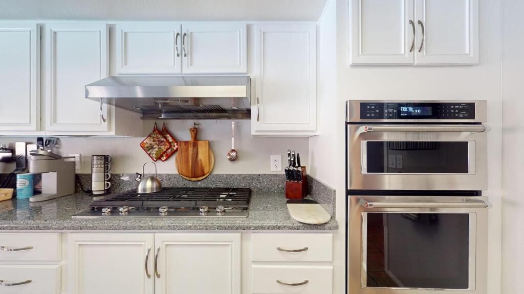 A modern kitchen with white cabinets, a stainless steel range hood, a double oven, and a granite countertop.