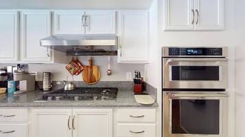 A modern kitchen with white cabinets, a stainless steel range hood, a double oven, and a granite countertop.