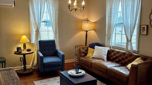 A cozy living room with a blue armchair, a brown leather sofa, a wooden coffee table, and a chandelier. - Quiet, Private Home in Kingston Springs for Two (Kingston Springs)