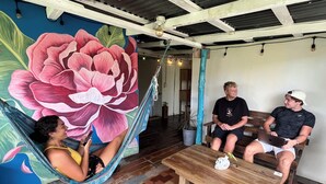 A room with a large floral mural, a hammock, a wooden bench, and a table. - The Bocas Corner Hostel (Bocas del Toro)