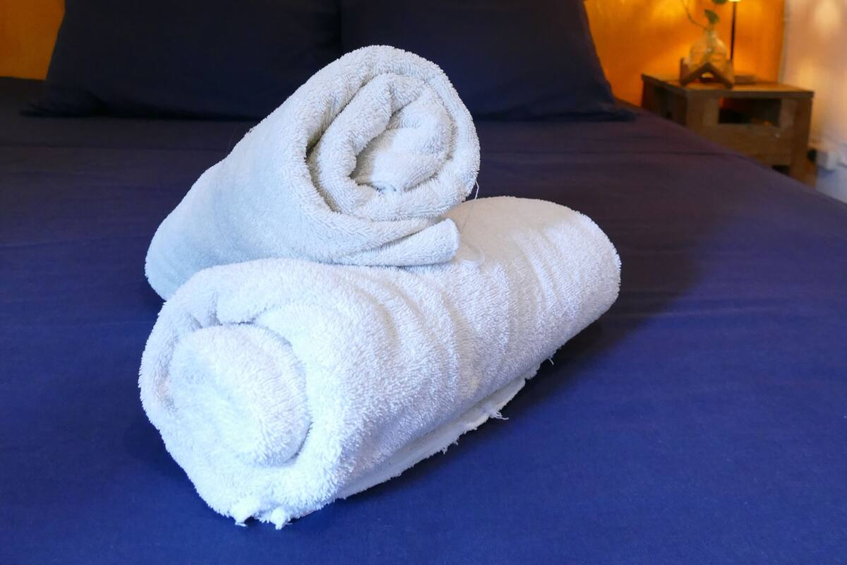Un lit bien fait, recouvert d’une couvre-lit bleue et agrémenté de deux oreillers foncés.