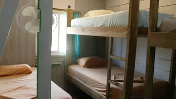Ein Schlafraum mit Etagenbetten, einem Ventilator, Holzwänden und einem Fenster mit Vorhängen.